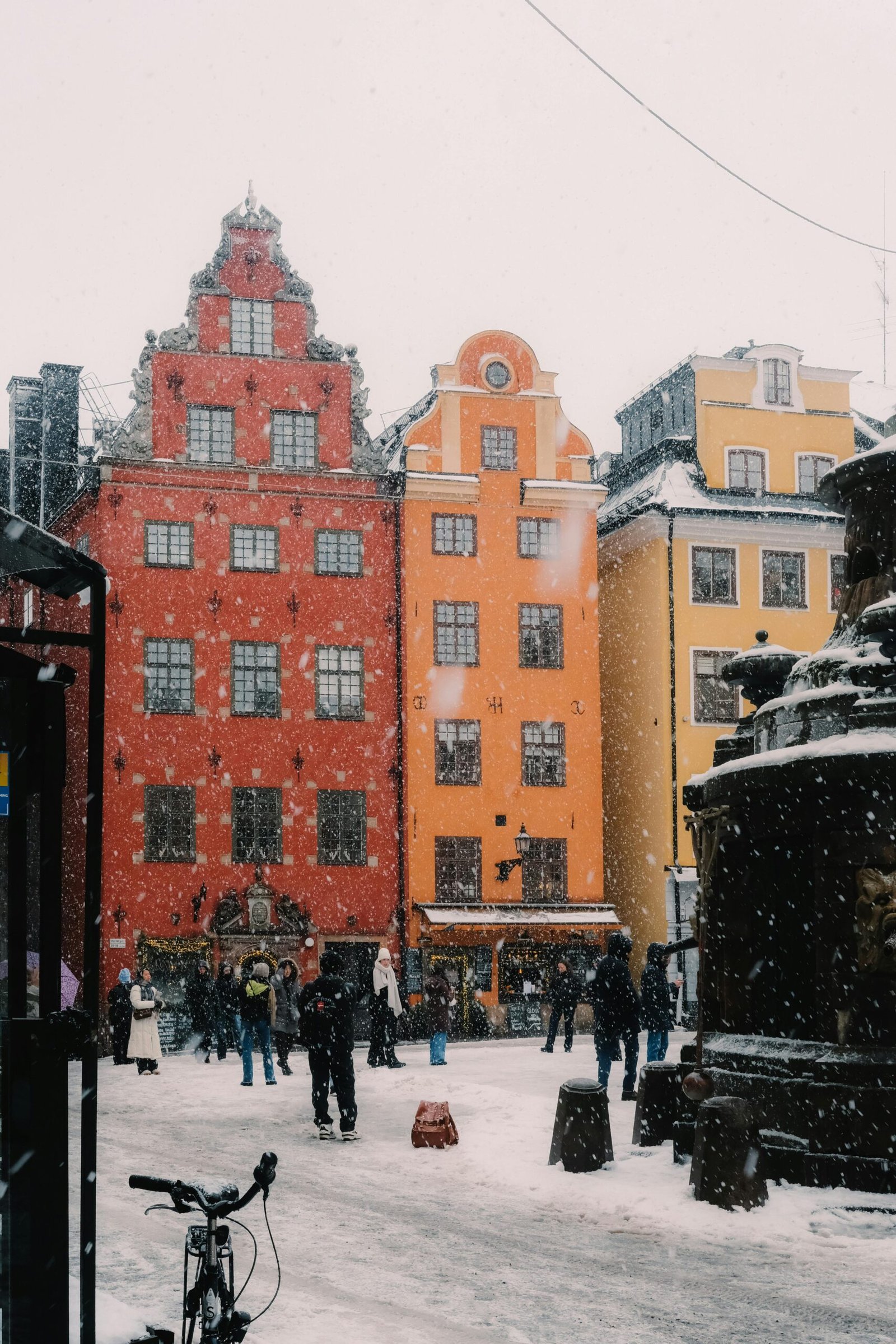 Snow falling in Swedish town with people outside.